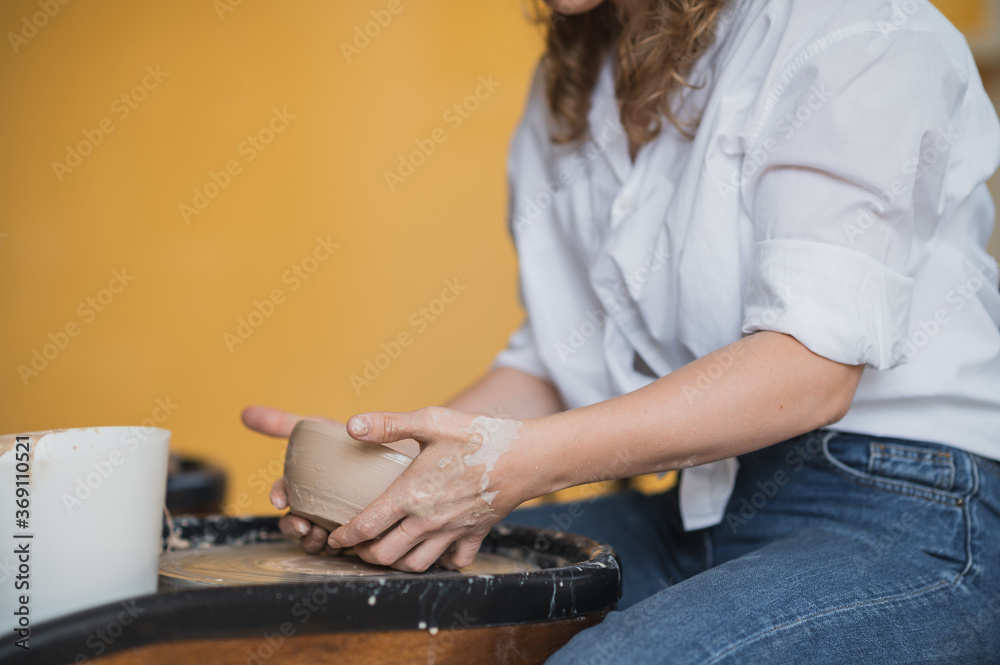 Close-up view of woman hands working on pottery wheel and making clay pot. Hands sculpts a cup from clay pot. Workshop on modeling on the potter's wheel