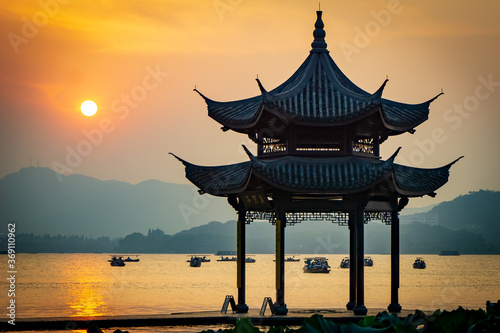 People watch the sunset on West Lake, a traditional Chinese pavilion with Chinese inscriptions. Translation: This place is for wise people to gather