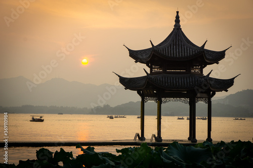 People watch the sunset on West Lake, a traditional Chinese pavilion with Chinese inscriptions. Translation: This place is for wise people to gather
