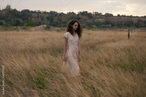 girl in a dress walks in a field with yellow grass
