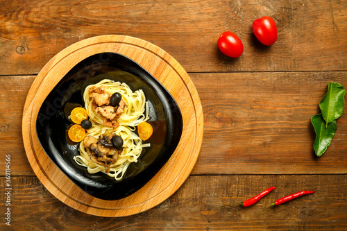 Black plate with spaghetti nests stuffed with assrty chicken fillet and mushrooms on a stand. Copy space