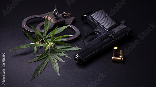 Cannabis leaves marijuana, weapons and handcuffs on dark background.