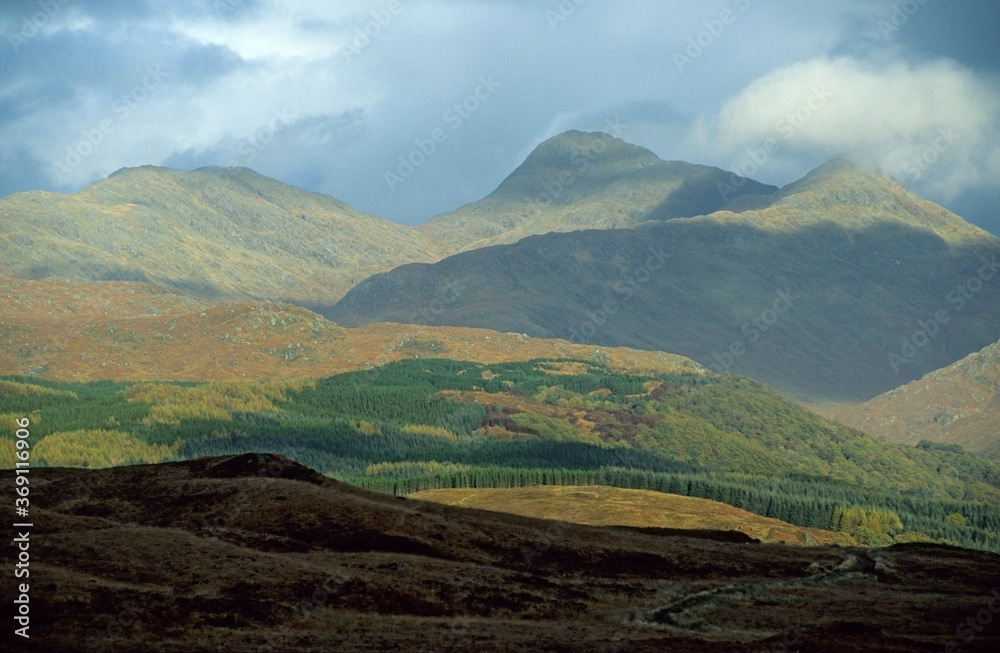 Scottish Highlands UK Autumn. Mountainous region with yellow moorland and dense green forests. Low lying white clouds on summit. Sunshine reflected on the hillsides. Slight mist on horizon.
