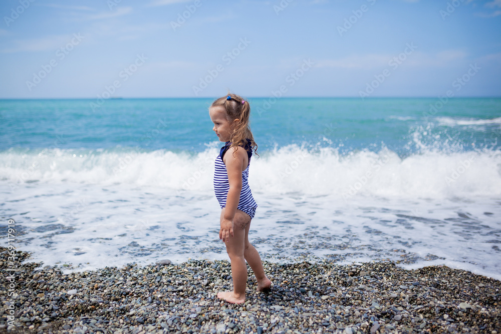 toddler 3-4 year old girl in a striped swimsuit runs to swim in the sea ...