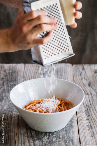 Anonymous cook rubbing cheese on spaghetti in sauce photo