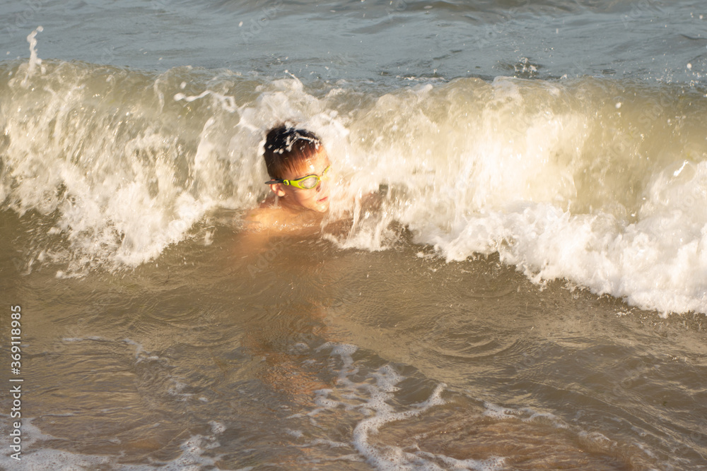Boy 10 years old enjoys swimming in the coastal waves in the sea.