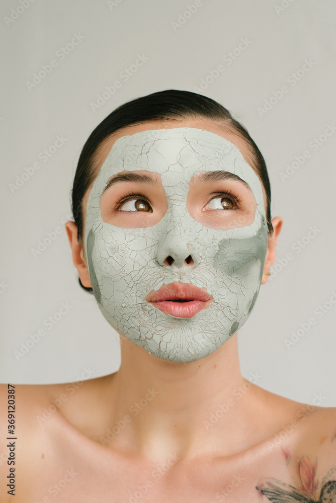 Closeup portrait of a charming Asian girl with a clay mask on her face and interesting emotion Closeup portrait of a charming Asian girl with a clay mask on her face and interesting emotion