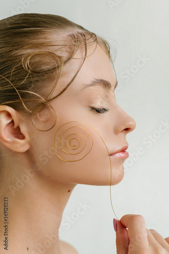 Closeup profile portrait of a cute blond girl with closed eyes and the curl wire in her hand ner the cheek and curls from the hair photo