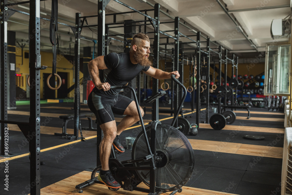 Strong and healthy man working out on a air bike, inside a crossfit gym. Strong and healthy man working out on a air bike, inside a crossfit gym.
