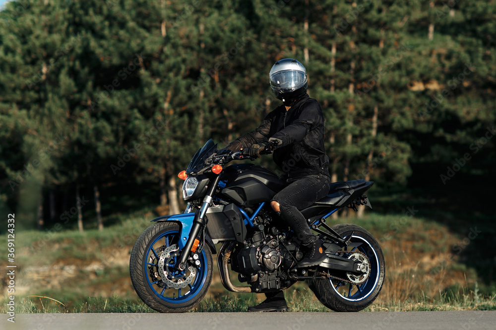 Photo of biker sitting on motorcycle in sunset on the country road. Photo of biker sitting on motorcycle in sunset on the country road.