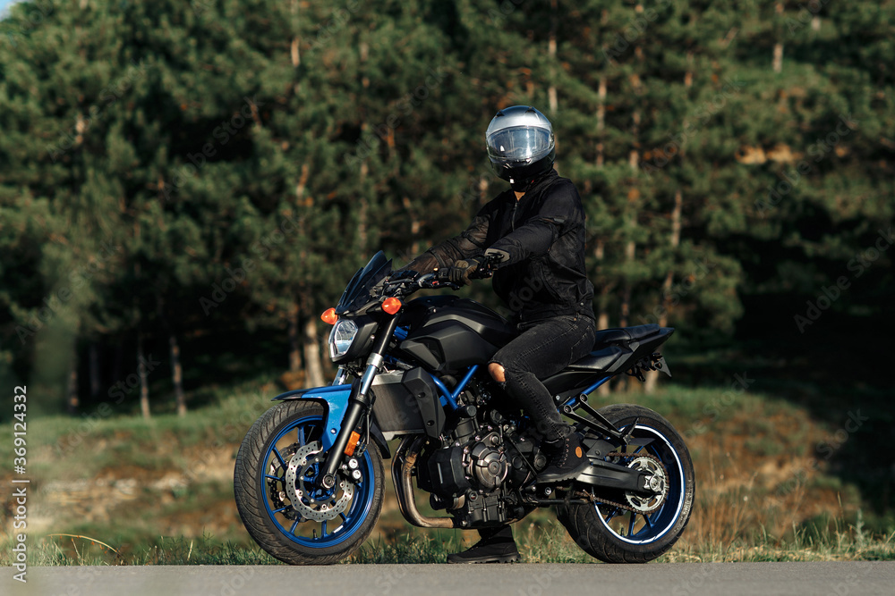 Photo of biker sitting on motorcycle in sunset on the country road.