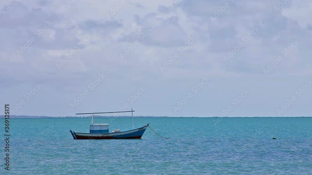Artisanal fishing boat anchored in the cove of Coroa Vermelha beach, blue and calm sea, sky with clouds Artisanal fishing boat anchored in the cove of Coroa Vermelha beach, blue and calm sea, sky with clouds