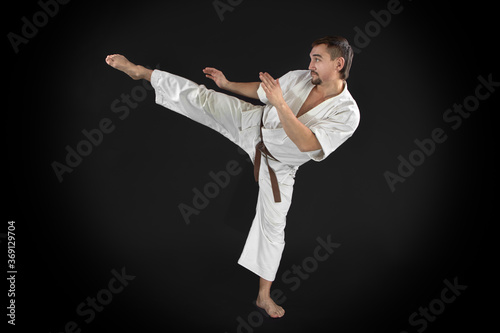 karate man training in-flight kick and posing on black background