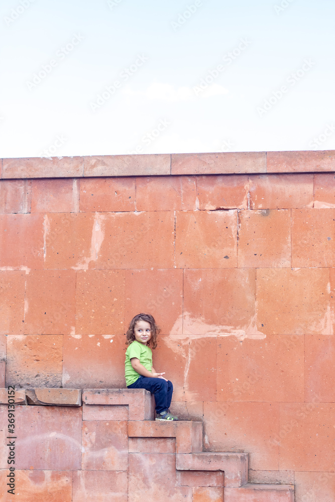portrait of a little long hair boy near the wall on stairs