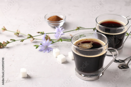 Chicory beverage in two glass cups, with concentrate and flowers on grey background. Healthy herbal beverage, coffee substitute