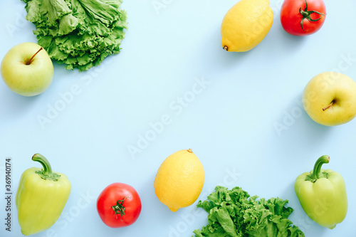 Fototapeta Naklejka Na Ścianę i Meble -  Various fresh vegetables and fruits on blue background. Ingredients for cooking. Frame from tomatoes, peppers, lemons, apple and lettuce