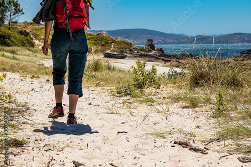a female hiker with a backpack walks on the sand with the sea on the lighthouses trail