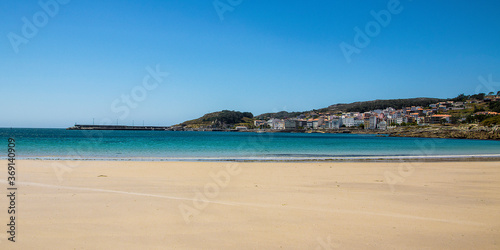 wide beach with fine sand and the calm blue sea in the background and the town of corme. Ermida Beach