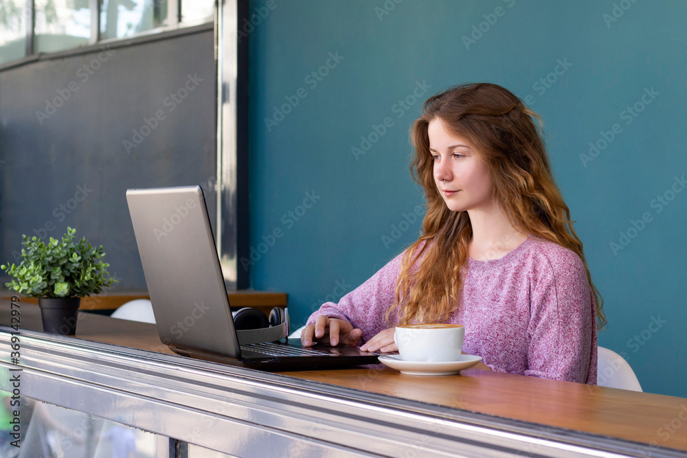 girl works for a laptop. remote work, online. girl in a cafe with a cup of coffee girl works for a laptop. remote work, online. girl in a cafe with a cup of coffee