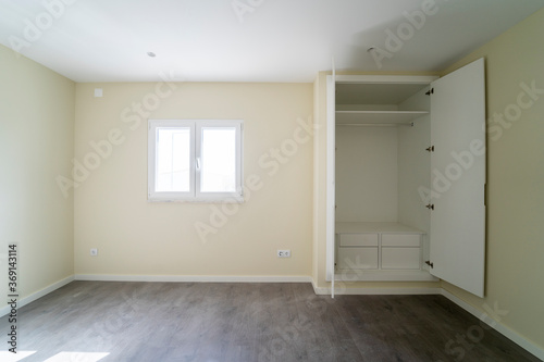 Empty room with dark wooden floating laminate flooring and wardrobe. House interior  wide bedroom space. Newly recently painted new apartment or house. Wood floor. Real state and property management