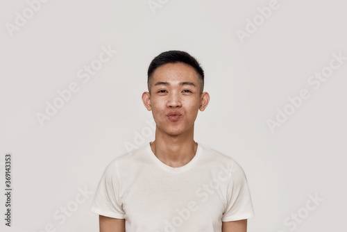 Kiss. Portrait of young asian man with clean shaven face looking playful while blowing, giving a kiss at camera isolated over white background. Beauty, skincare, facial expression