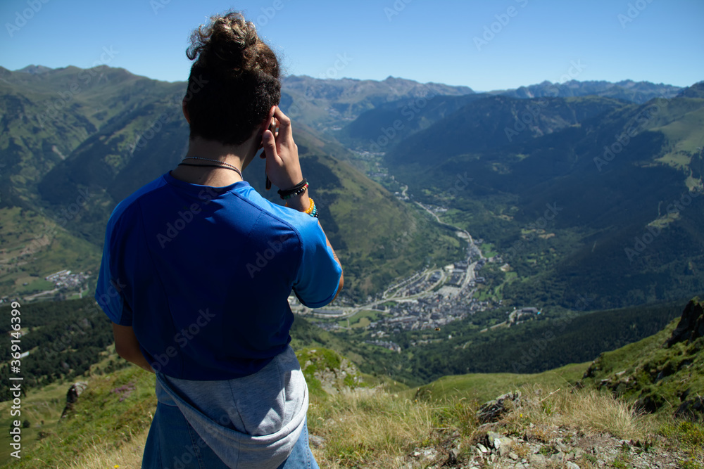 Hiker in the mountains, young man looking at the horizon and talking on the smartphone from the top of a mountain in summer.