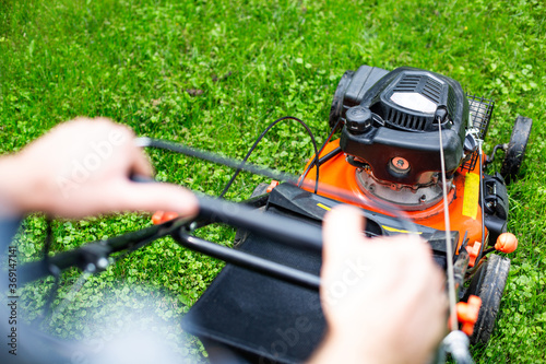 Gardening. Mowing a lawn with a gasoline lawnmower, close-up on male hands on a lawn mower handle.