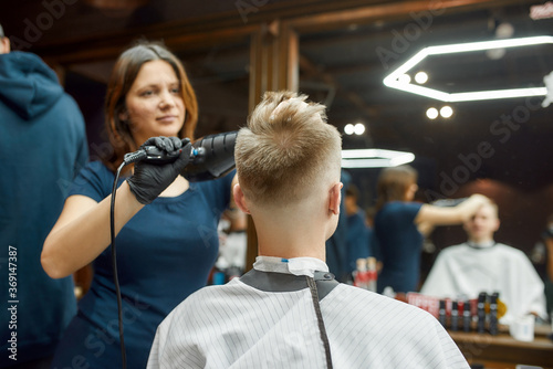 Barbershop. Professional young barber girl drying hair of a young guy sitting in barbershop chair in front of the mirror