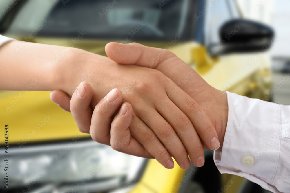 Woman buying car and shaking hands with salesman against blurred auto, closeup Woman buying car and shaking hands with salesman against blurred auto, closeup
