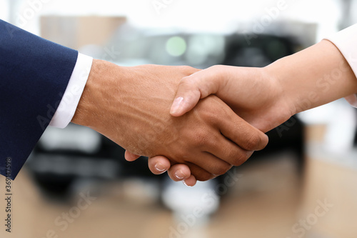 Woman buying car and shaking hands with salesman against blurred auto, closeup