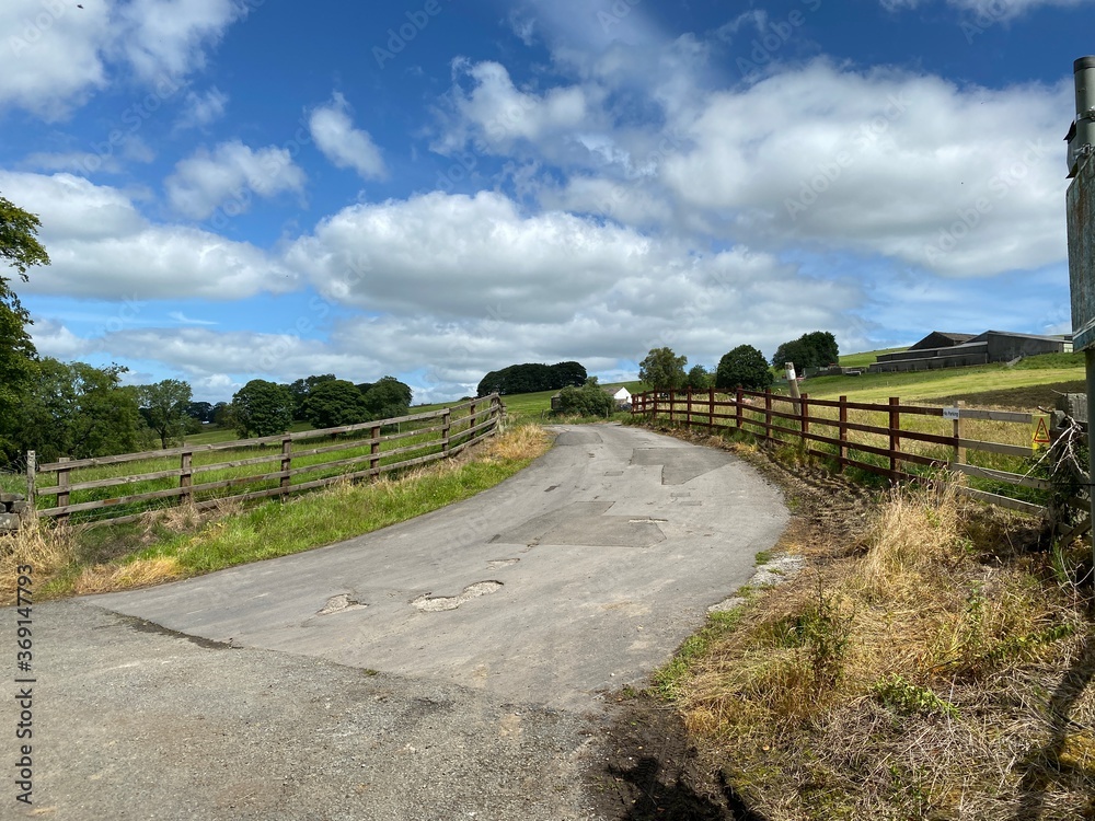 Country road, with wooden fencing, leading over the hill, past fields and meadows in, Trawden, Colne, UK 