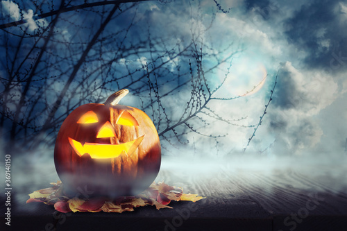 Spooky Jack O Lantern pumpkin surrounded by mystical mist under full moon on Halloween. Space for text
