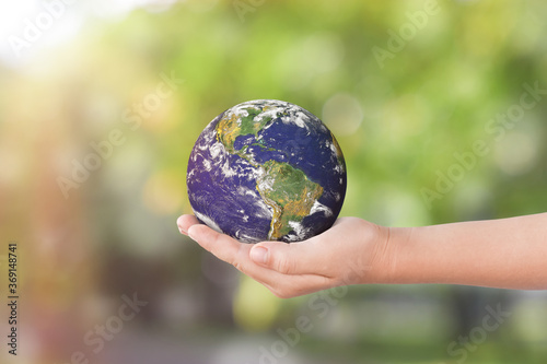 Environment day concept: Child hands holding earth over blurred green nature background. Elements of this image furnished by NASA