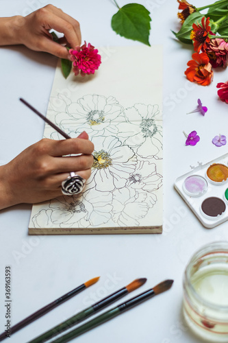 Anonymous female artist painting flowers with watercolors on a sketch pad