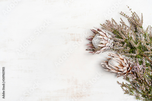 Beautiful flat lay floral arrangement including beautiful dried pink King Proteas and delicate thryptomene flowers, on a white rustic background.