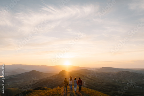 group of people stands in mountains and watches how the sun sets photo