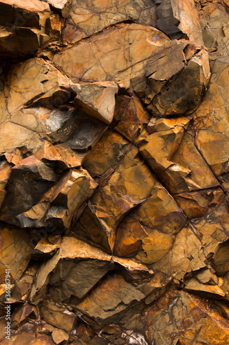 Wall of orange and copper colored jagged and fractured stones near basaltic intrusions