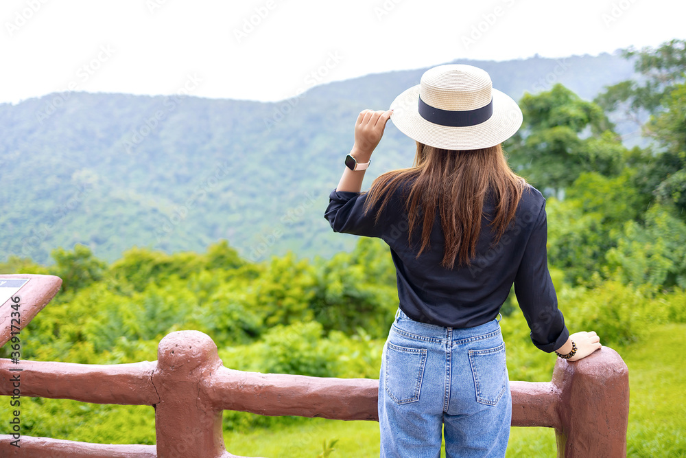Woman wearing a hat, black shirt, blue jeans standing looking mountian view.