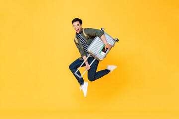 Young excited Asian tourist man with baggage jumping in mid-air ready to travel isolated on yellow background