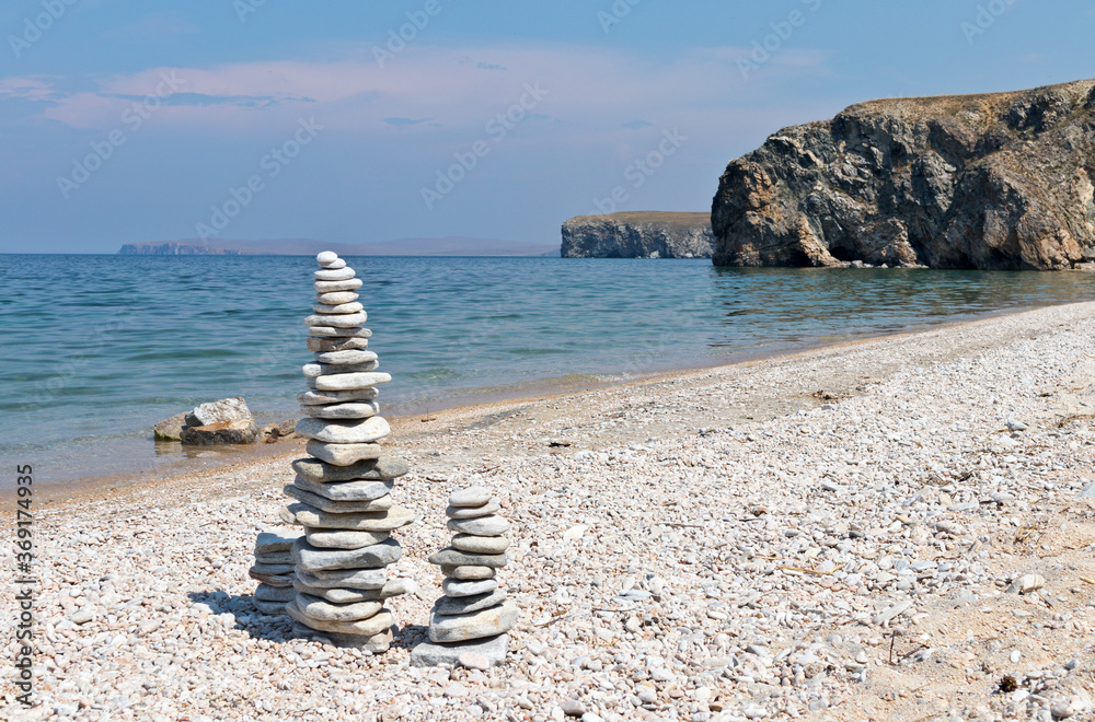 Baikal Lake at sunny summer day. Beautiful beach with tourists stone pyramids on the shore of Olkhon Island. Natural background. Holidays by the lake and travel around the island