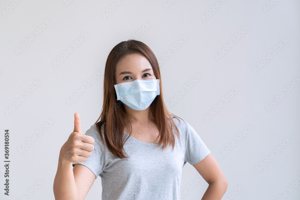 Portrait of cheerful young Asian girl with protective face mask thumb up posing and smiling at camera over white background. Copy space