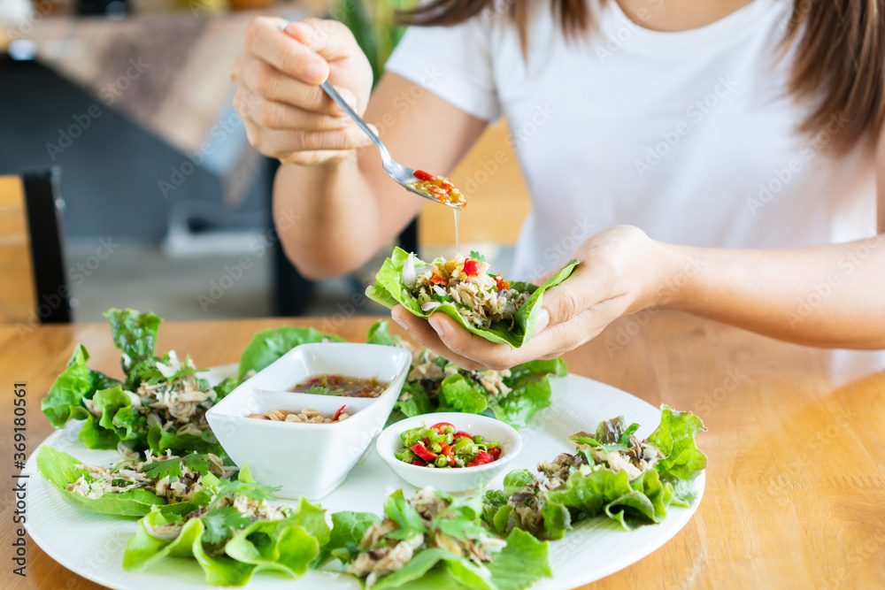 Close up of woman eating fried mackerel spicy salad served with fresh vegetable, chilies, peanut and Thai spicy Fish Sauce. This food is Thai traditional food call Maing-Pla-too menu. Close up