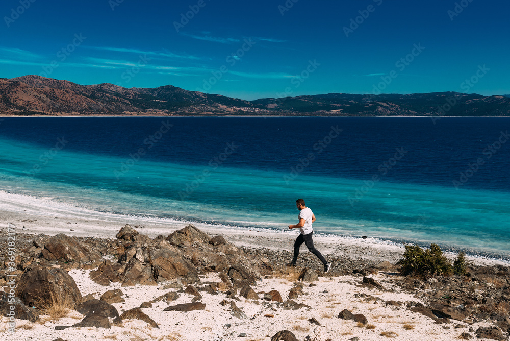 A man walks along the shore of lake Salda in Turkey. A man runs along the shore. A man runs along the beautiful coast of lake Salda in Turkey. Copy space