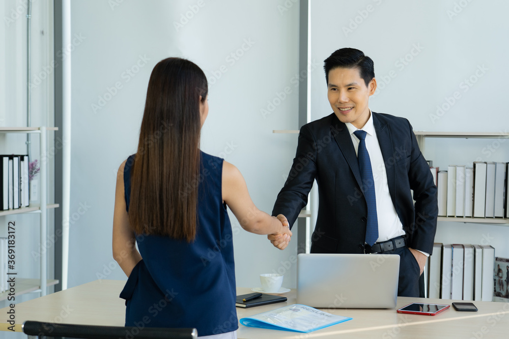 Asian Business woman and asian business man handshaking over the table, on the desk that has a computer and application documents Asian Business woman and asian business man handshaking over the table, on the desk that has a computer and application documents