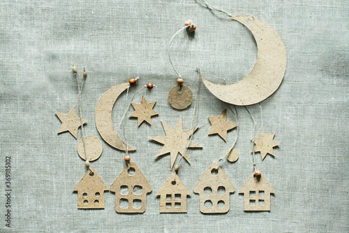 Handmade Christmas decorations flat lay on a canvas background. Cardboard decorative stars, small houses and crescent moon.