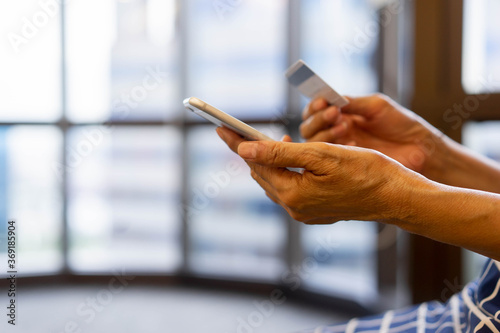 close up senior woman hand using smartphone and holding credit card to paying bills from shopping online concept