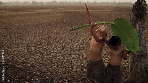 Climate change, Asian boys enjoy with first falling rain season on dry cracked land. Environment conservation and stop global warming concept