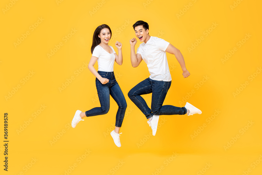 Full length portrait of lovely Asian couple smiling and jumping in mid-air isolated on yellow background Full length portrait of lovely Asian couple smiling and jumping in mid-air isolated on yellow background