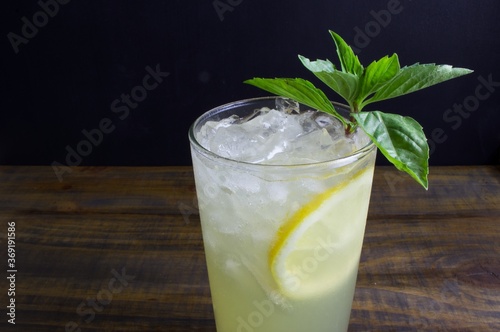 Iced gin basil cocktail with lemon garnish isolated against a dark wood background with space for copy