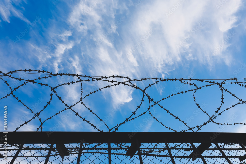 Fence with barbed wire against blue sky Fence with barbed wire against blue sky